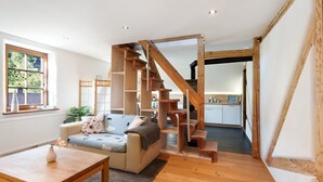 Een modern interieur met een houten trap, een bank, een bijzettafeltje en uitzicht op het exterieur.