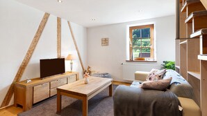 Un salon moderne avec un téléviseur, des meubles en bois, une fenêtre donnant sur un beau paysage et un escalier.