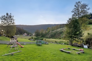 A playground with a slide and swings, surrounded by a grassy field and trees, with houses in the background. - Apartment 'Familienwohnung Simba' with Mountain View, Shared Garden and Wi-Fi (Forbach)