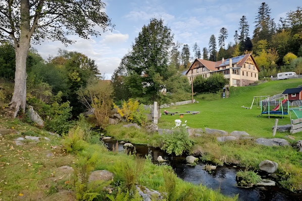 Una casa con jardín, un pequeño arroyo y un parque infantil.
