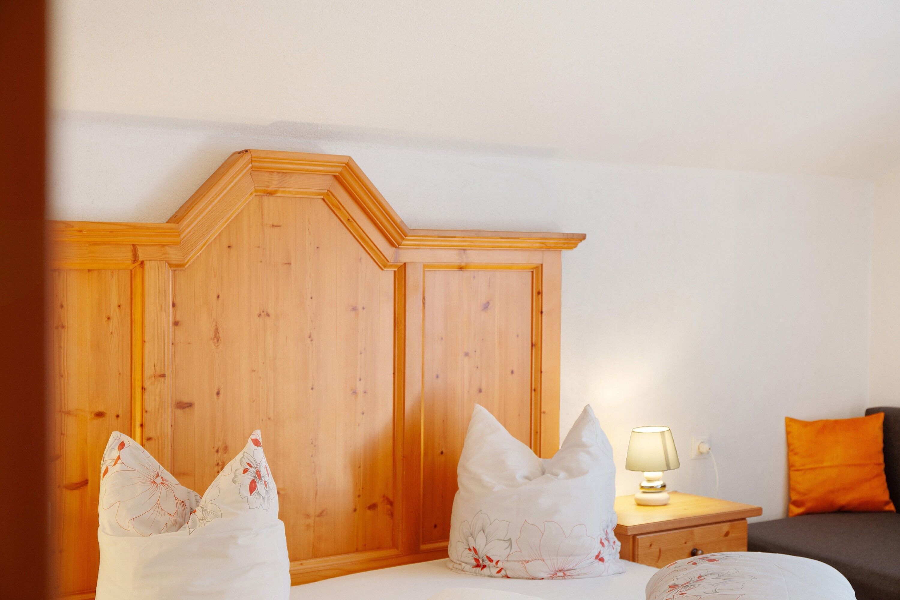 A bedroom with a wooden headboard, a bedside table with a lamp, and a bed with floral pillows.