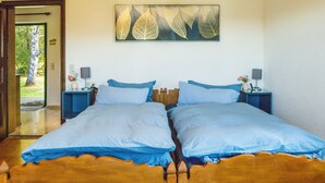 A double bed with blue bedding, two bedside tables with lamps, a wall-mounted artwork of leaves, and a door leading to a garden.