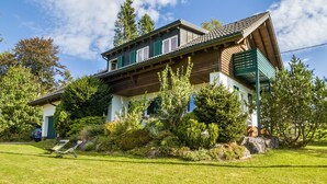 A two-story house with a sloped roof, green shutters, and a well-maintained garden with various shrubs and a lawn.