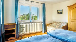 Une chambre avec deux lits, un radiateur, une fenêtre avec des rideaux, une chaise et une porte.