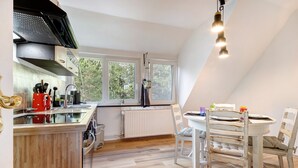 A kitchen with a wooden countertop, a dining table with chairs, a radiator, and a window with a view of trees.