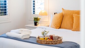A neatly made bed with white linens and a blue throw, a basket of breakfast items, and a lamp on a bedside table. - The Beach Bach – Peaceful and relaxing villa (Vincentia)