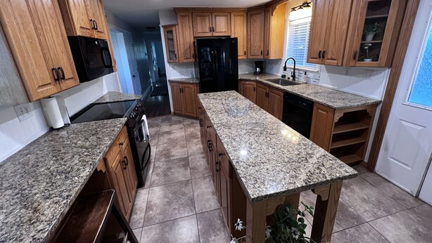 A kitchen with wooden cabinets, granite countertops, a black refrigerator, and a window with blinds. - Split Mountain View Paradise! Life on the farm! (Vernal)
