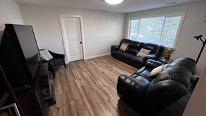 A living room with a black leather sofa, a television, and a wooden floor. - Split Mountain View Paradise! Life on the farm! (Vernal)