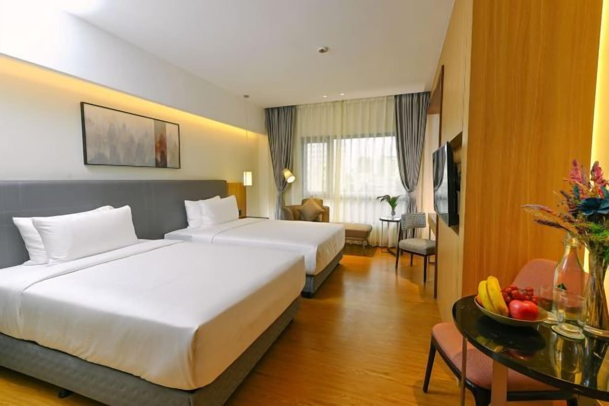 A hotel room with two beds, a dining table with fruit, a vase with flowers, and a television.