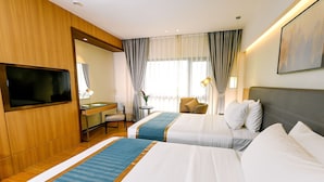 Quarto de hotel com duas camas, uma escrivaninha, televisão e uma cadeira.