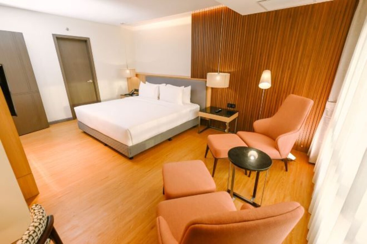 A modern hotel room with a large bed, two bedside tables, a chair, and a small table.
