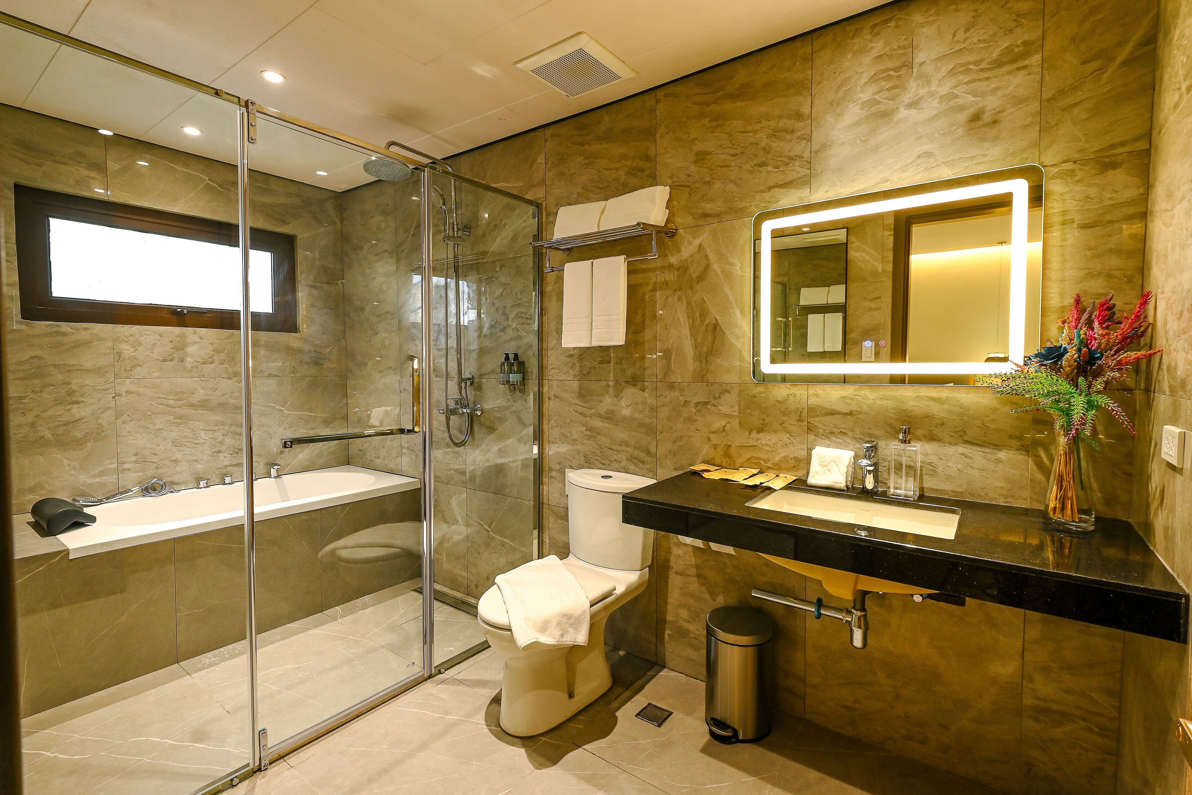 Une salle de bain moderne avec une douche à parois de verre, des toilettes, un lavabo avec un miroir et une poubelle.