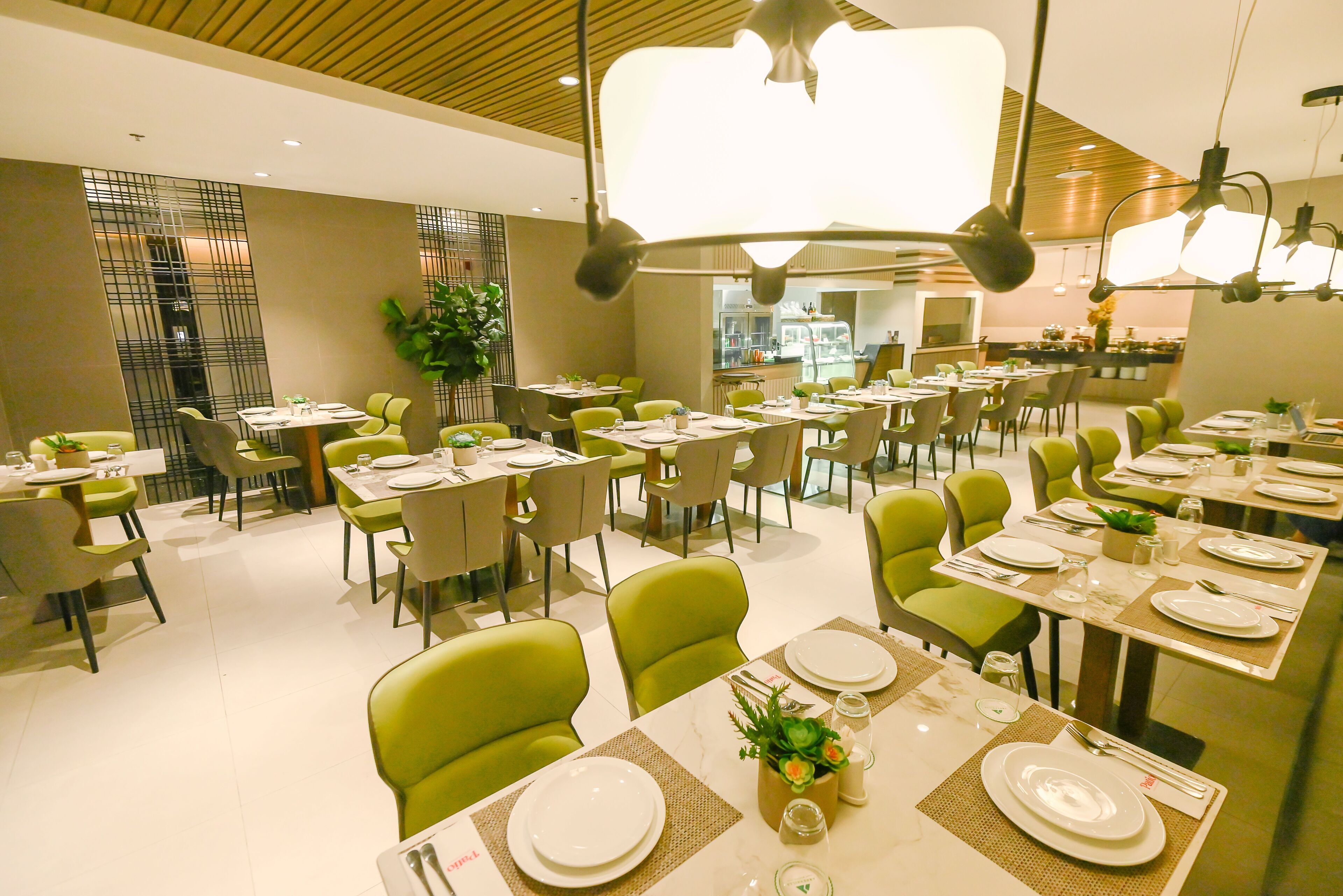 A modern dining area with green chairs, white tables, and a central plant.