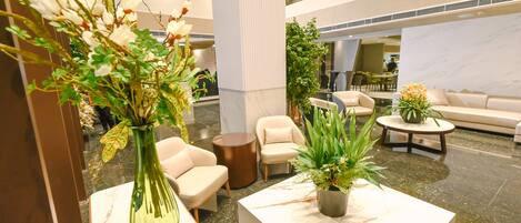 A modern lobby with marble flooring, a reception desk, comfortable seating, and decorative plants.