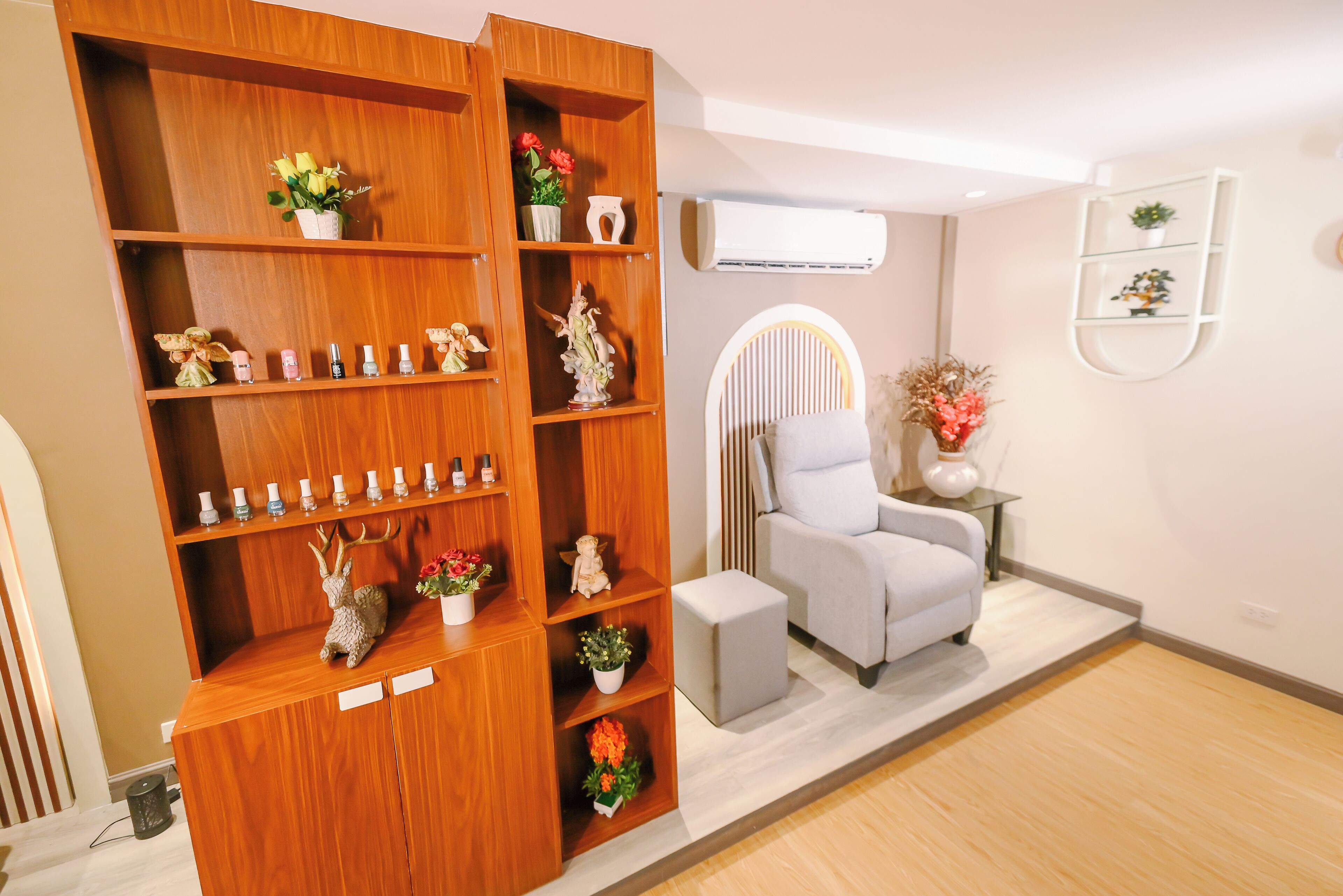 A room with a wooden bookshelf, a grey armchair, a small table with a vase, and an air conditioning unit on the wall.