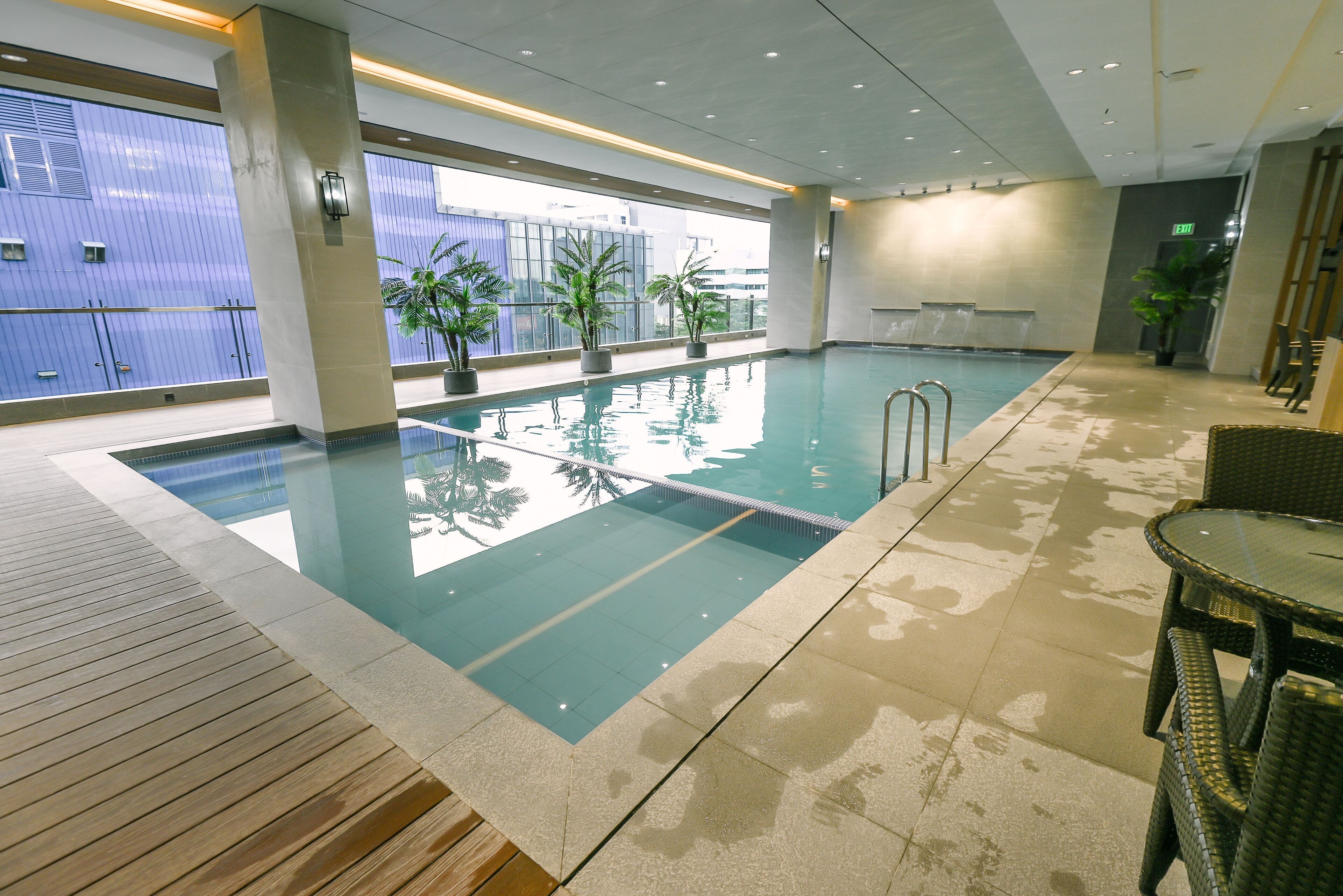 Une piscine intérieure à l’eau claire, dotée d’une terrasse en bois et agrémentée de plantes en pot.