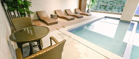 Zona de piscina con mobiliario de mimbre y una mesa de vidrio.