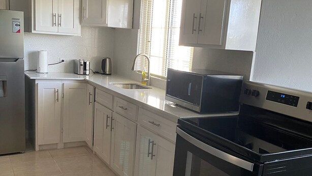 Una cocina moderna con gabinetes blancos, un refrigerador de acero inoxidable, un microondas, un tostador y un horno negro.