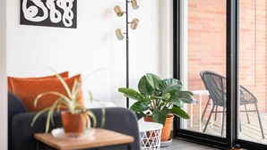 A modern living room with a sofa, a coffee table, and two potted plants. There is a floor lamp and a window with a view of a brick wall and outdoor furniture. - Pine Tree House 316 (Traverse City)