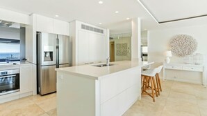 A modern kitchen with white cabinetry, a large island, stainless steel appliances, and a view of the sea.