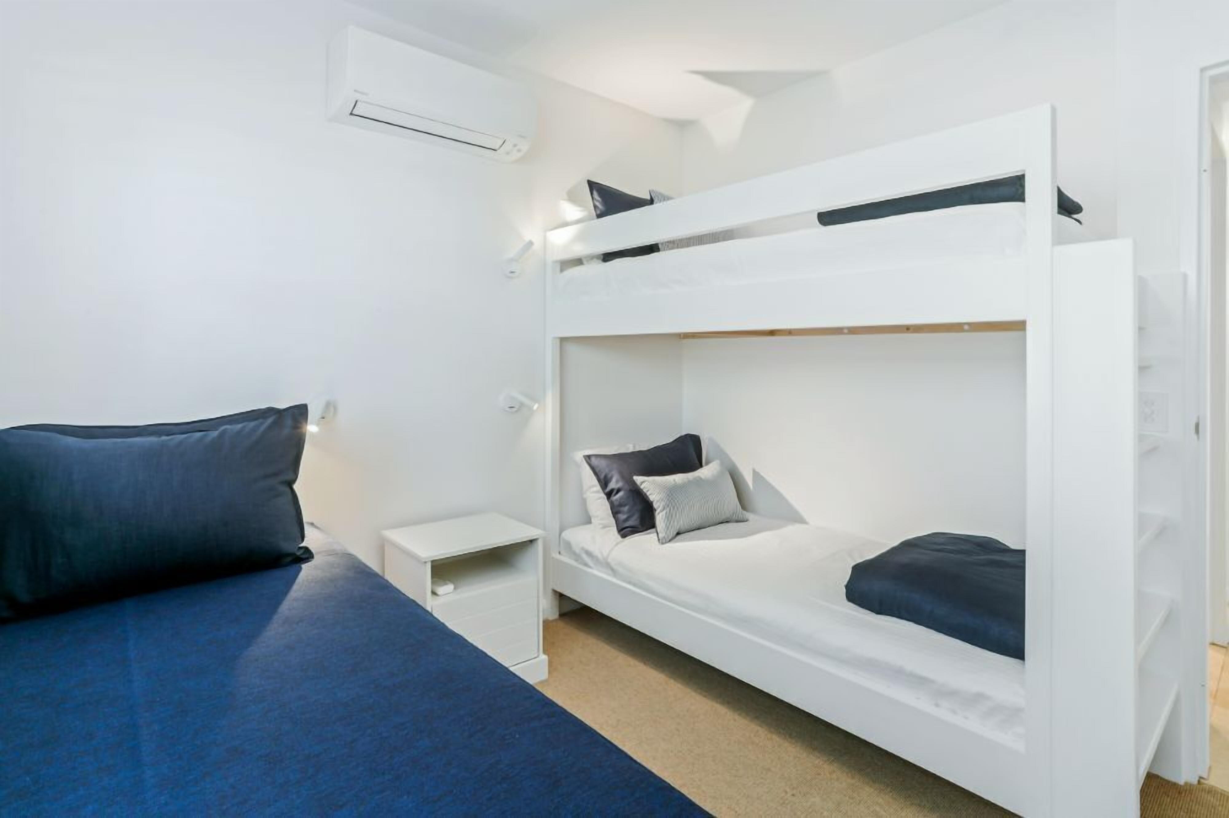 Ein Schlafraum mit Etagenbetten, einer weißen Wand, einem kleinen Nachttisch und einer blauen Bettdecke.