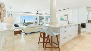 A modern kitchen with white cabinetry, a central island with bar stools, and a view of the outdoors.
