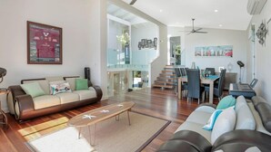 A spacious living area with a sofa, coffee table, and a dining area with chairs and a table. There is a staircase leading to another level. - The Lighthouse on Noosa Hill (Noosa Heads)