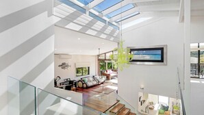 A modern interior with a glass staircase, a living area with a sofa and a dining table, and a view of the outdoors. - The Lighthouse on Noosa Hill (Noosa Heads)