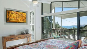 A bedroom with a large bed, a wooden dresser, a painting, and a balcony with a view. - The Lighthouse on Noosa Hill (Noosa Heads)