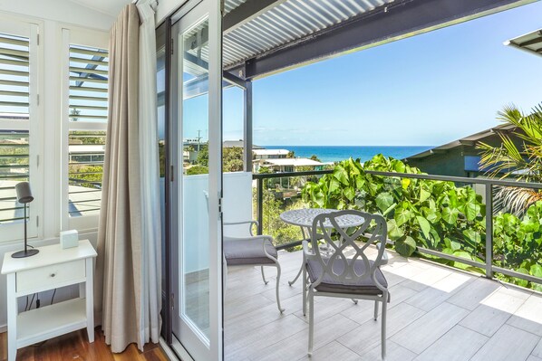 Enjoy the ocean view from this balcony with a table, chairs, and lush green surroundings.