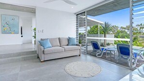 Sala de estar moderna com um sofá cinzento, um tapete redondo e uma porta de vidro que dá para uma varanda com área de estar ao ar livre.