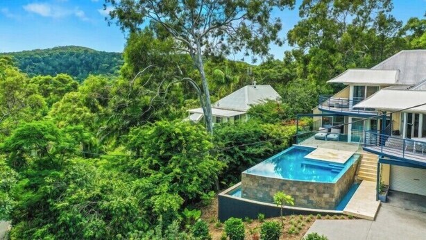 A modern house with a swimming pool surrounded by lush greenery and hills in the background.