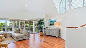 A spacious living area with a large window, a sofa, a side table, and a staircase.