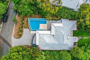 Vista aérea de una casa con piscina, rodeada de abundante vegetación y un césped cuidado.