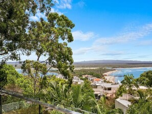 A coastal hotel with a view of the ocean, surrounded by greenery and a clear sky.