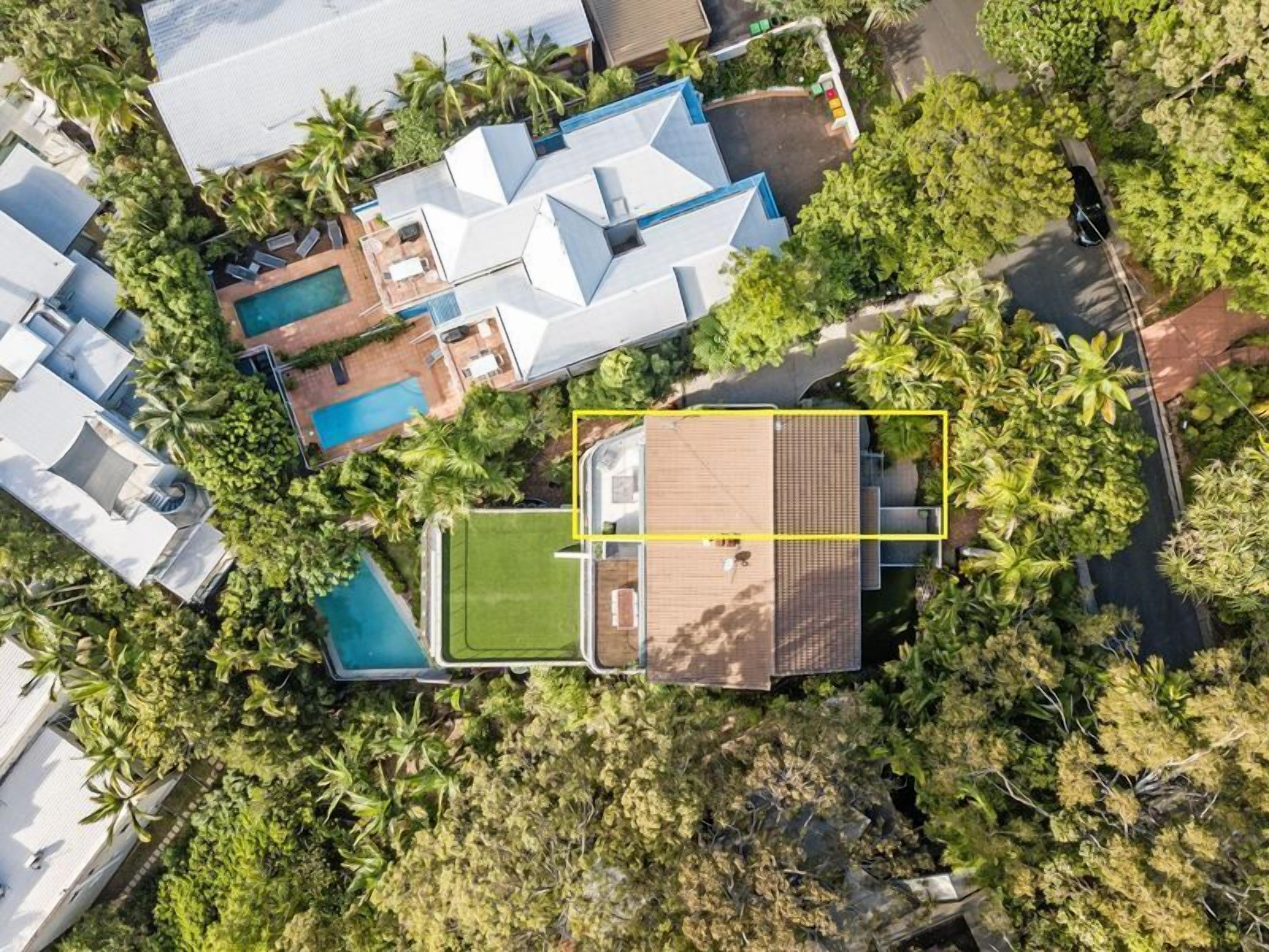 Luchtbeeld van een modern huis met zwembad, overdekt terras en weelderige begroeiing.