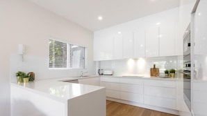 Una cocina moderna con armarios blancos, una isla central y un ventanal con persianas.