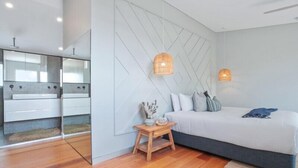 A modern bedroom with a bed, bedside tables, and a wall-mounted light fixture. - Luxe Coastal Abode, Marcus Beach (Marcus Beach)