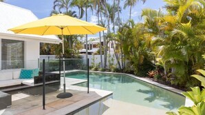A swimming pool with a yellow umbrella, a white building, and palm trees. - Peaceful Holiday Living in Noosa Heads (Noosa Heads)