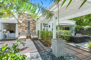 Relax in a serene outdoor space surrounded by lush greenery and a pergola, featuring a seating area and wicker chairs.