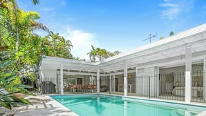 Zona junto a la piscina con un porche cubierto, piscina y vistas del entorno verdeado.