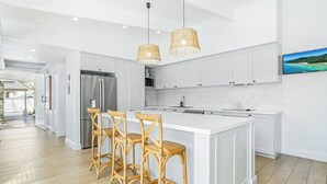 Una cocina moderna con armarios blancos, una isla grande con taburetes de bar, electrodomésticos de acero inoxidable y un revestimiento de baldosas en patrón de espiga.