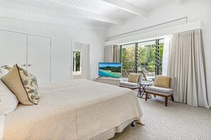 Relax in this serene hotel room with a large bed, TV, and balcony overlooking lush greenery and a pool.