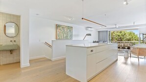 A modern kitchen with a central island, a dining area with wicker furniture, and a view of greenery outside.