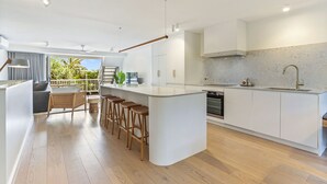 A modern kitchen with a central island, bar stools, a built-in oven, and a large window overlooking greenery.