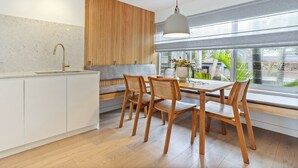 A modern kitchen with a wooden accent wall, a dining area with wooden chairs, and a large window offering a view of greenery.
