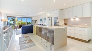 A modern kitchen with a central island, white cabinetry, and a view of the outdoors. - Comfortable & stylish with rooftop spa (Sunshine Beach)