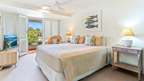 A bedroom with a large bed, a ceiling fan, a TV on a stand, a bedside table with a lamp, and a view of the outdoors through a sliding door. - Comfortable & stylish with rooftop spa (Sunshine Beach)