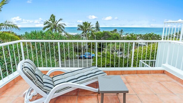 A balcony with a white railing, a striped lounge chair, and a small table. - Comfortable & stylish with rooftop spa (Sunshine Beach)
