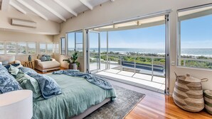 A bedroom with a large bed, a sofa, and a view of the ocean through a sliding glass door. - Indulge at Iluka, Castaways Beach (Noosa)